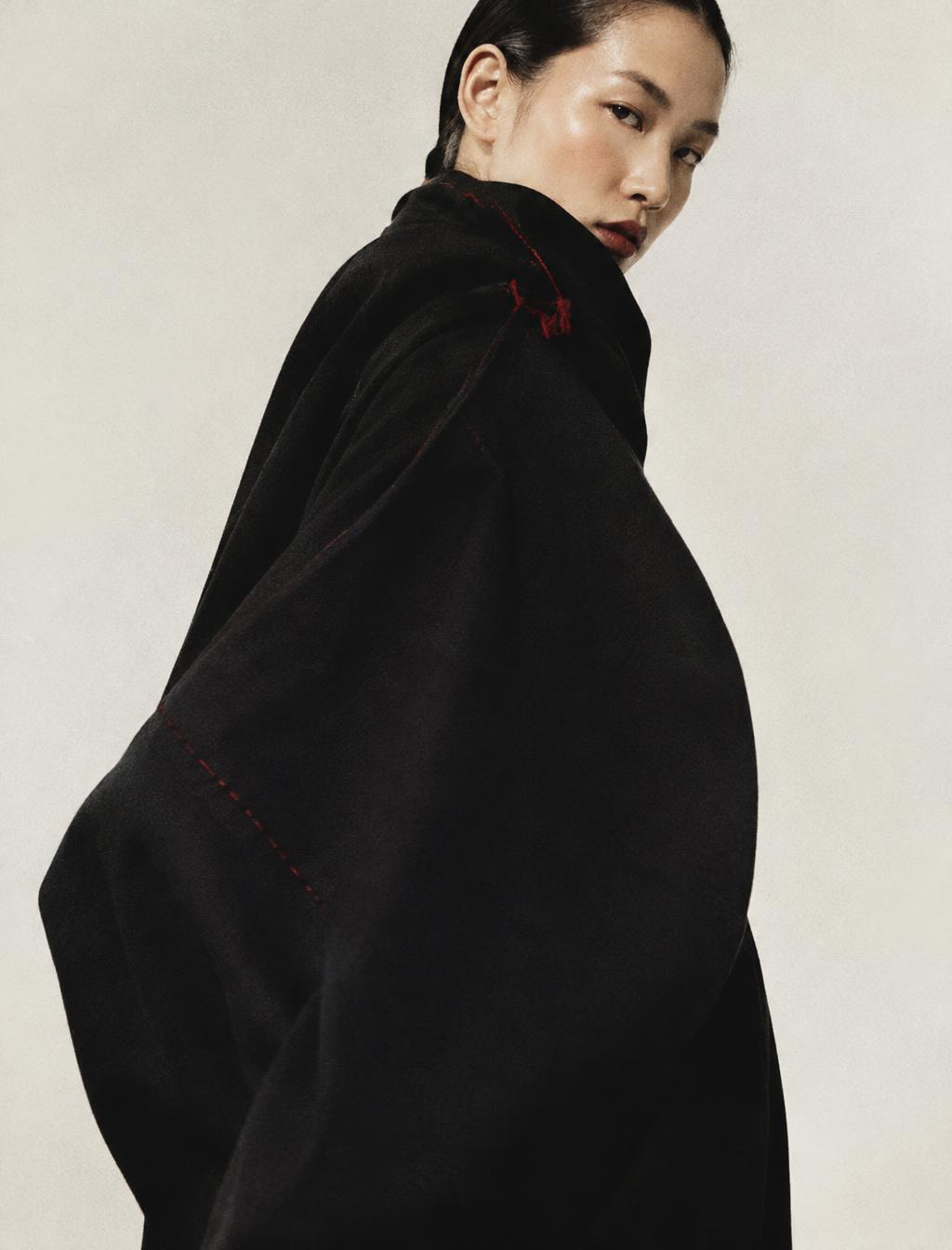 Model in an oversized black garment with red stitching